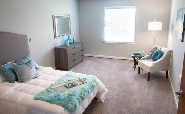 apartment bedroom with a large bed, chair, dresser and window