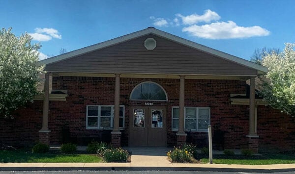 Outside image of Country Charm assisted living building with two trees on each side and a blue sky