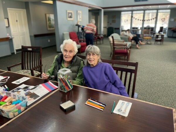 two senior women smile while doing crafts together