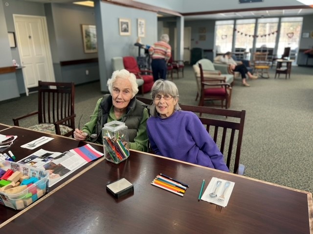Two senior women smile while doing crafts together