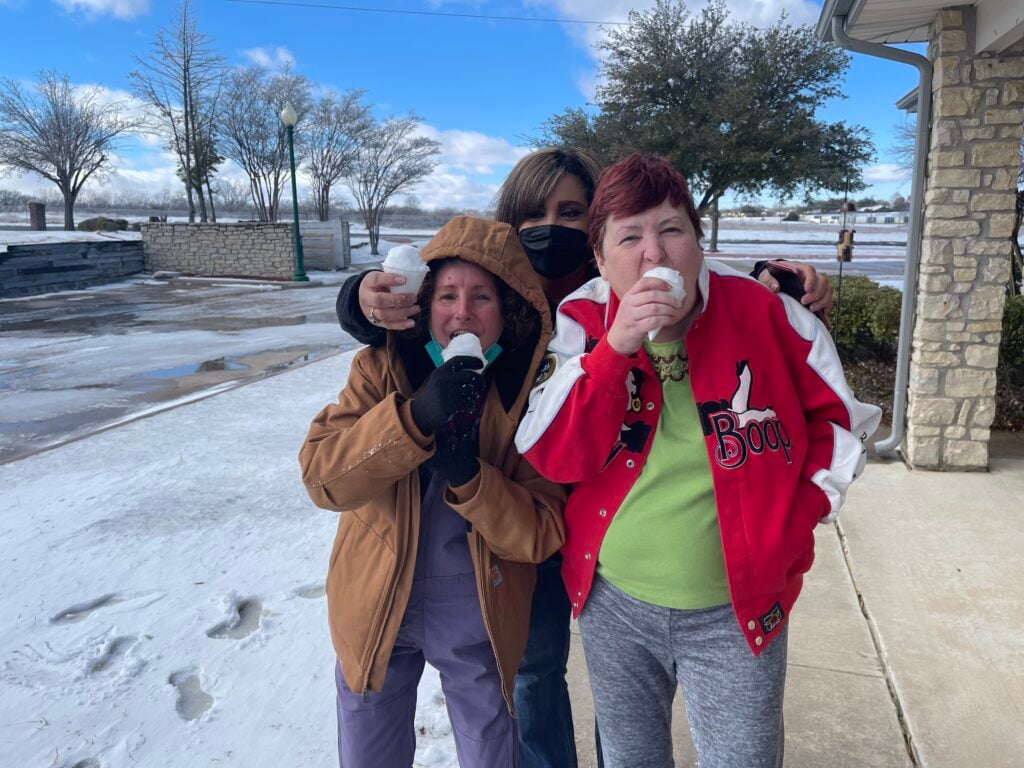 three women eat snow balls outside during winter storm