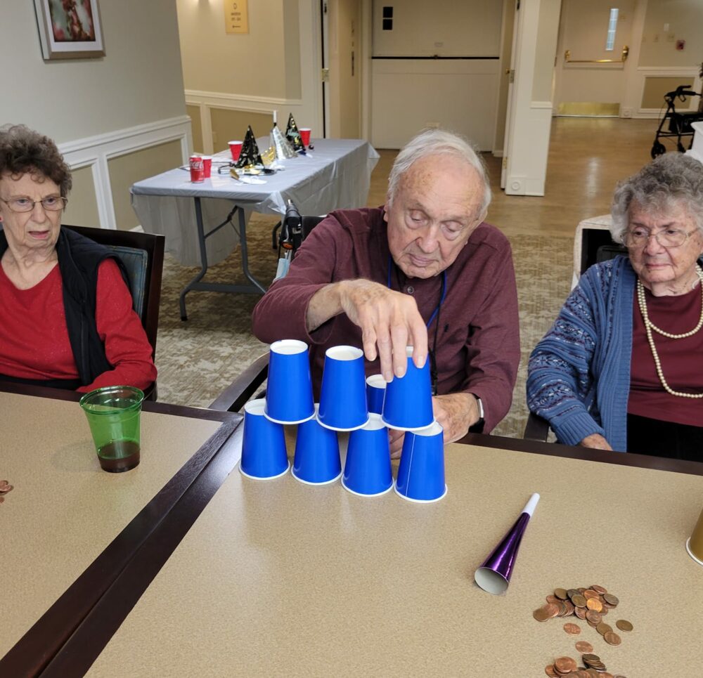 senior man stacks cups on top of each other while two senior women watch