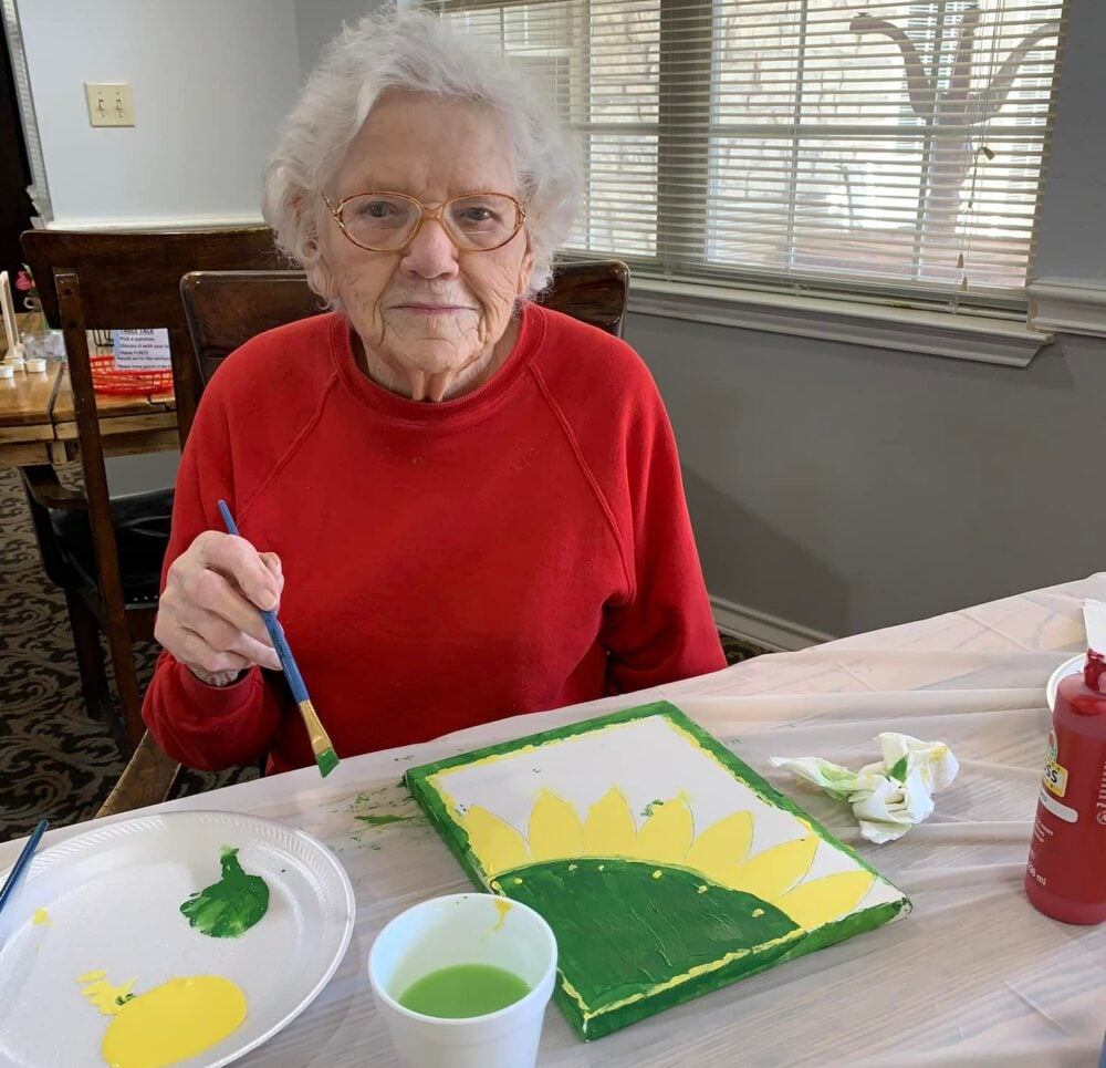 senior woman paints a picture of a green and yellow flower