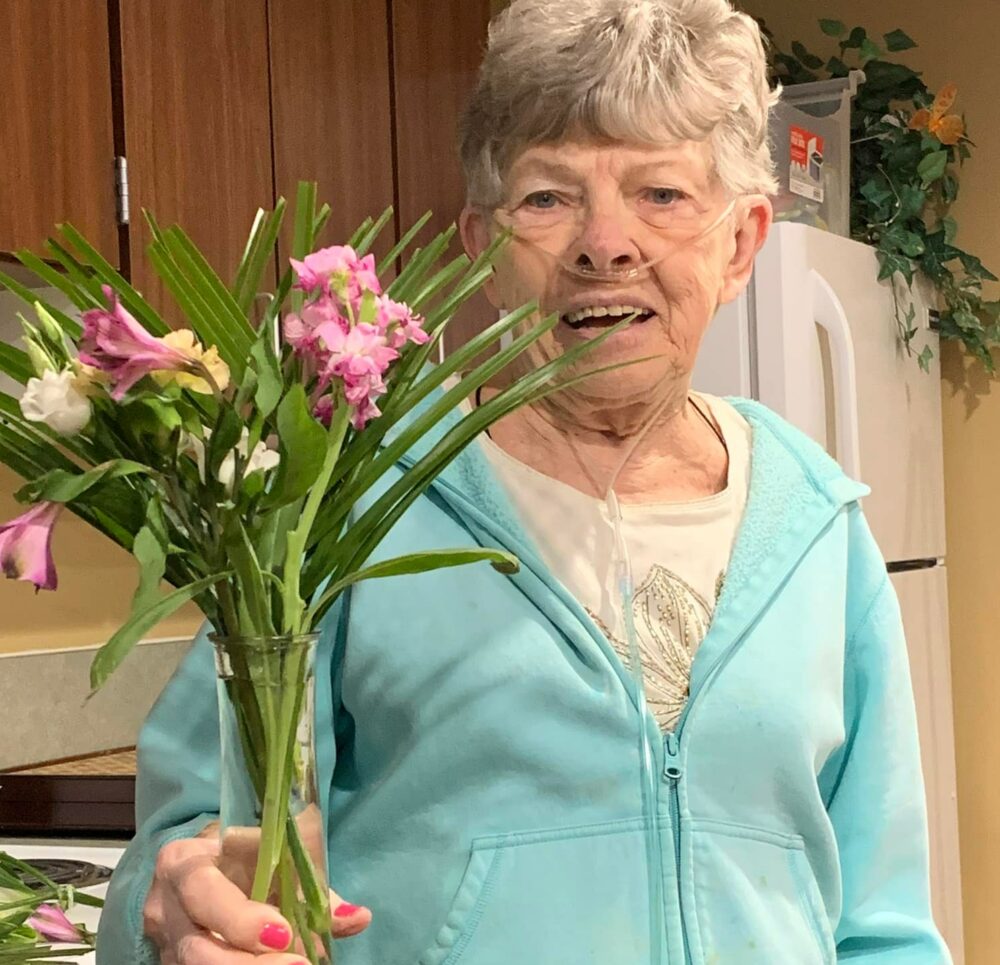 senior woman smiles with a bouquet of pink flowers