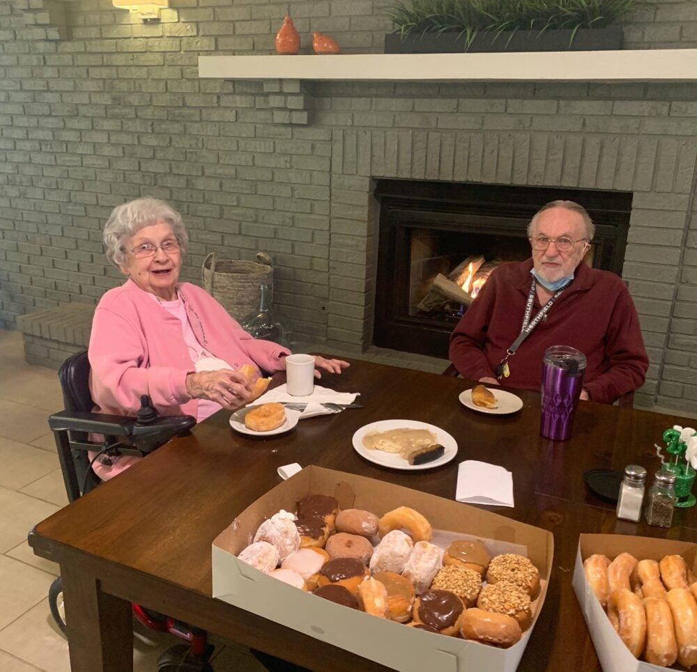 senior man and senior woman smile while eating donuts