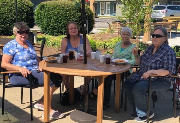 four senior women smile while eating outside on the patio