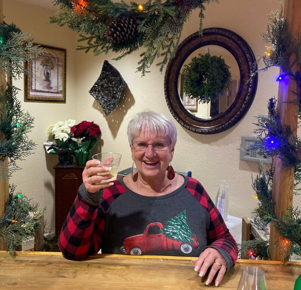 senior woman holds a drink and smiles while among Christmas decorations