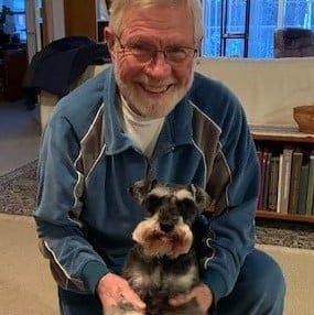 senior man smiles while holding his small black and white dog
