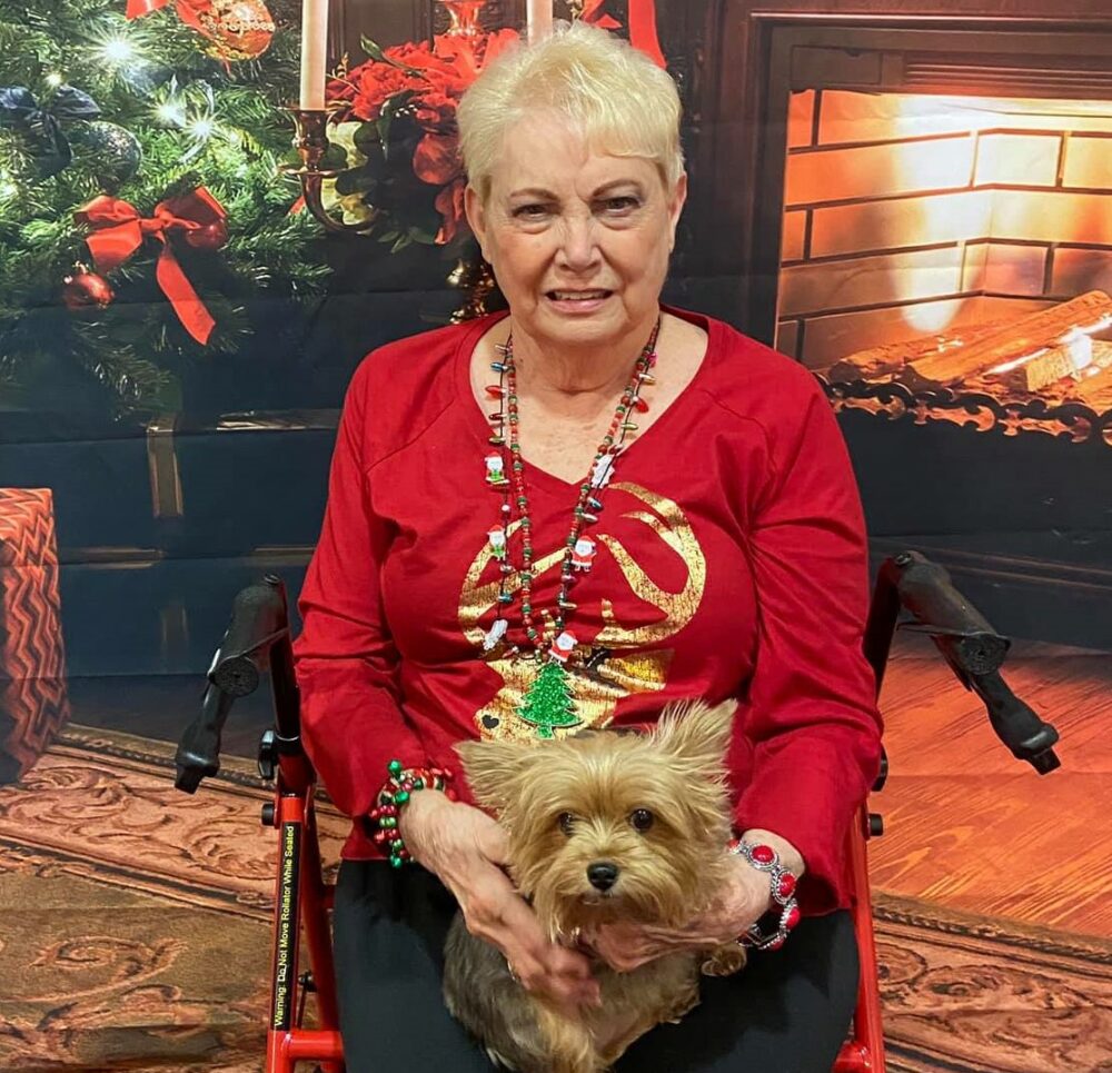 senior woman smiles with her little brown dog during Christmas