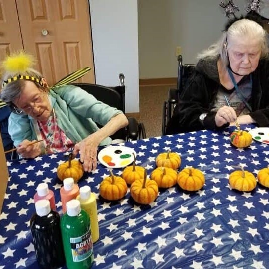 two senior women paint tiny pumpkins while wearing costumes