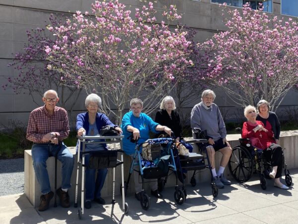 group of seniors sit outside a museum with purple trees in the background