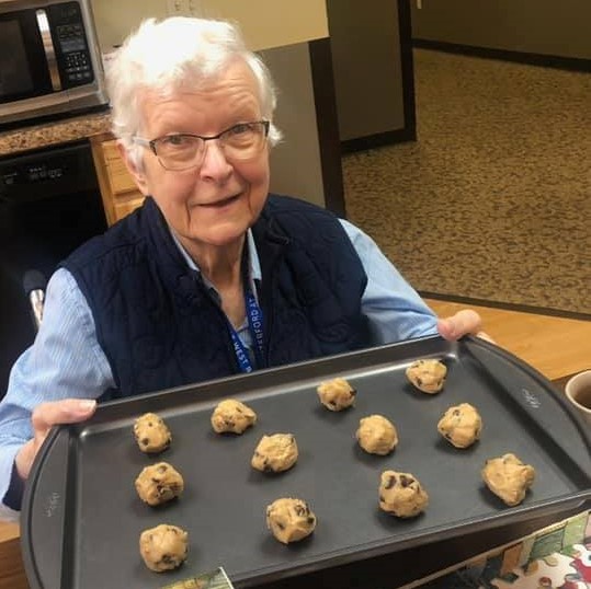 senior woman smiles while holding a tray of cookies before putting them in the oven