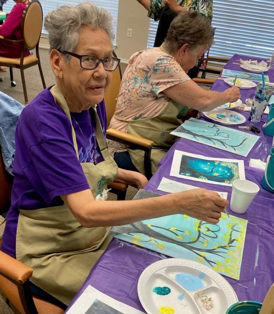 senior woman paints a picture of a forest during a guided class