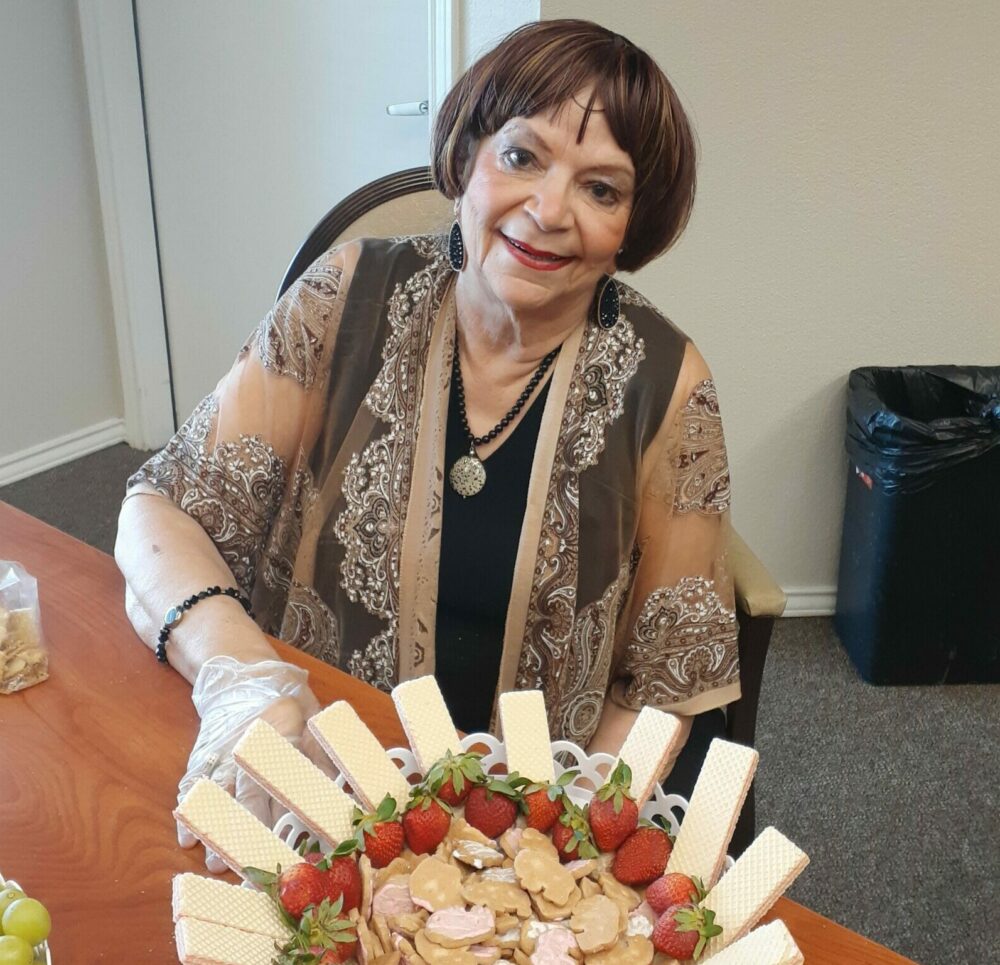 senior woman smiles while posing with a fruit platter