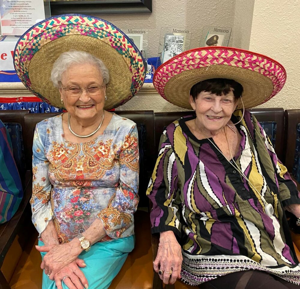 two senior women smile while wearing sombreros