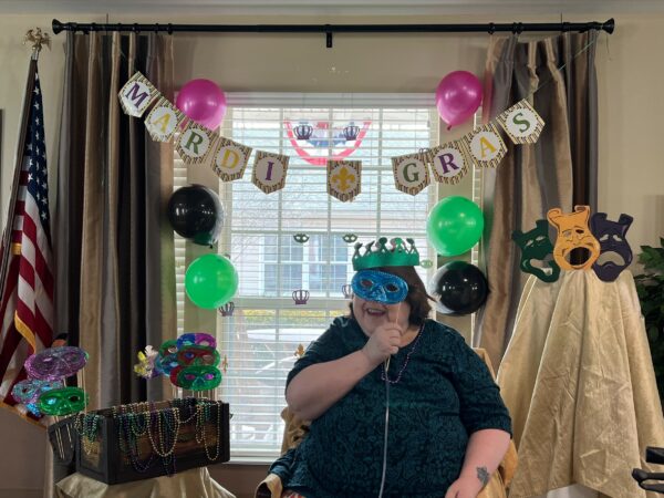 senior woman poses in front of a mardi gras display