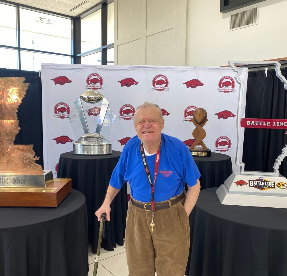 senior man smiles while standing beside award tables