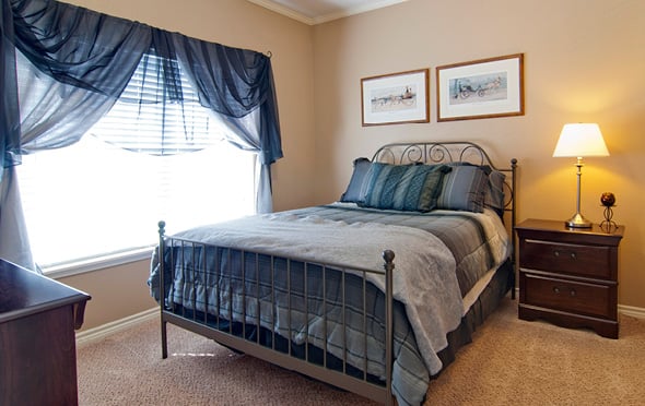 Senior apartment bedroom with a large bed, side table and dresser