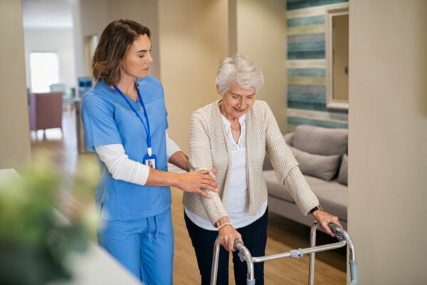 Young nurse helping senior patient using a walking frame to walk in hospital corridor
