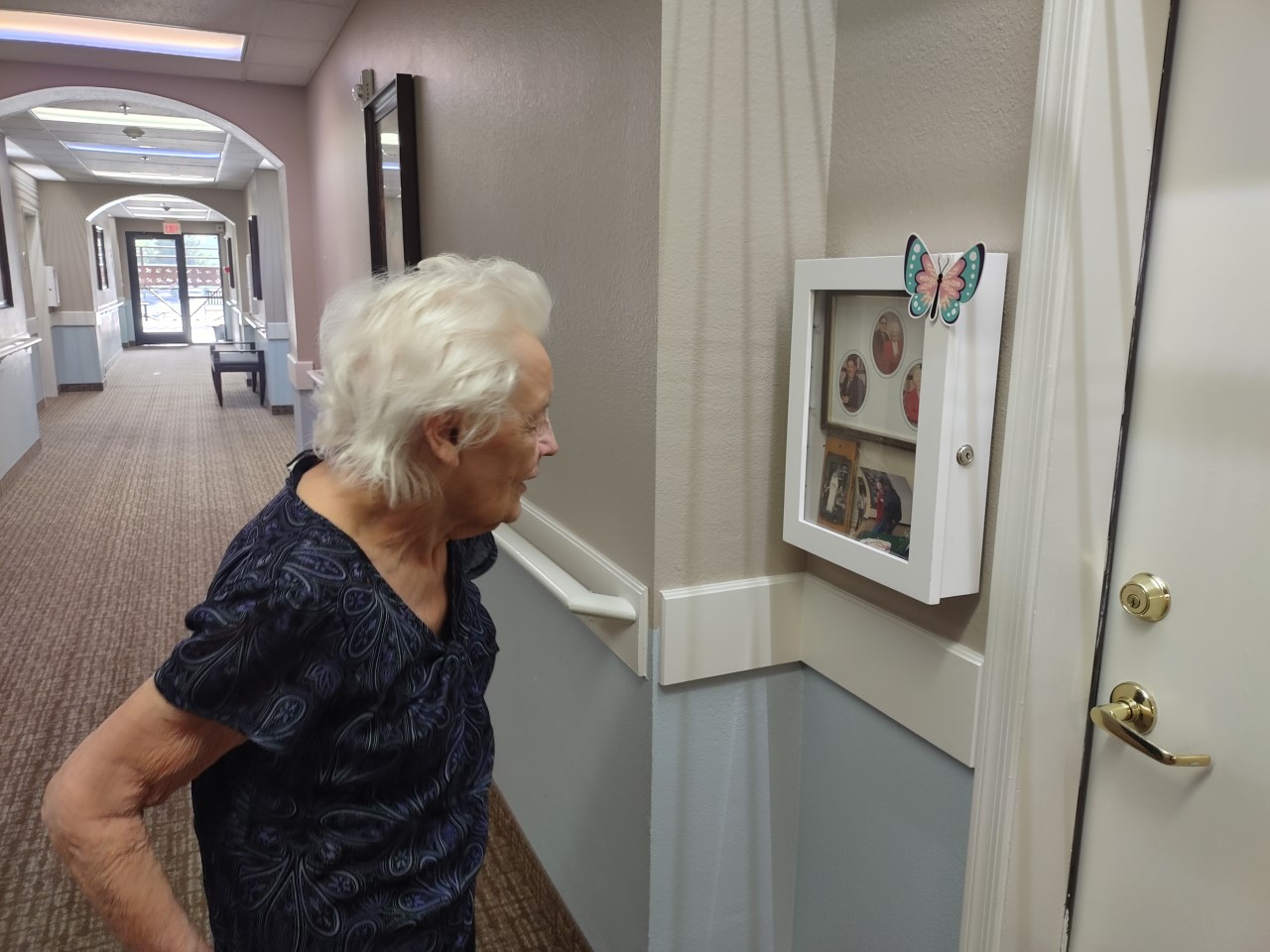 senior woman looks at a shadowbox outside of her apartment