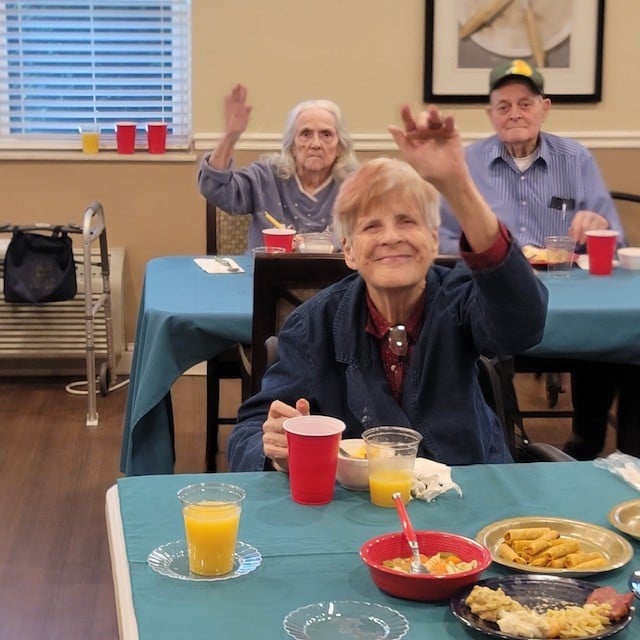 senior woman waves at the camera while eating a snack