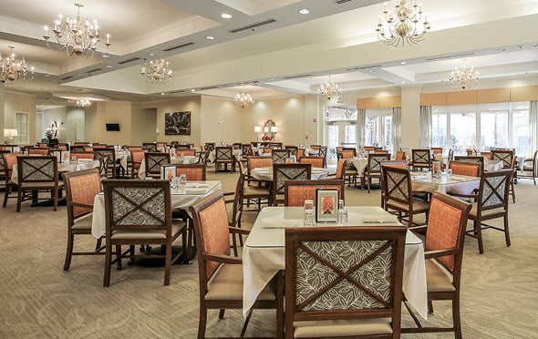 Dining room with many tables and chandeliers at a senior living community.