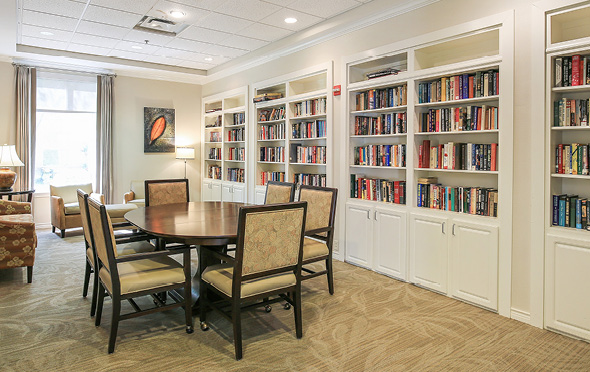 Library at a senior living community with table and chairs and rows of books.