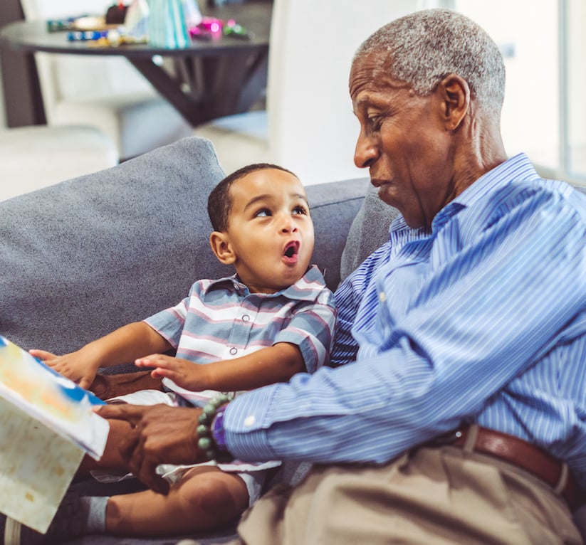 Older man reading to his grandson on the couch