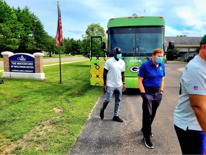 three men walk inside the facility of the waterford at wisconsin rapids with the green bay packers bus in the background