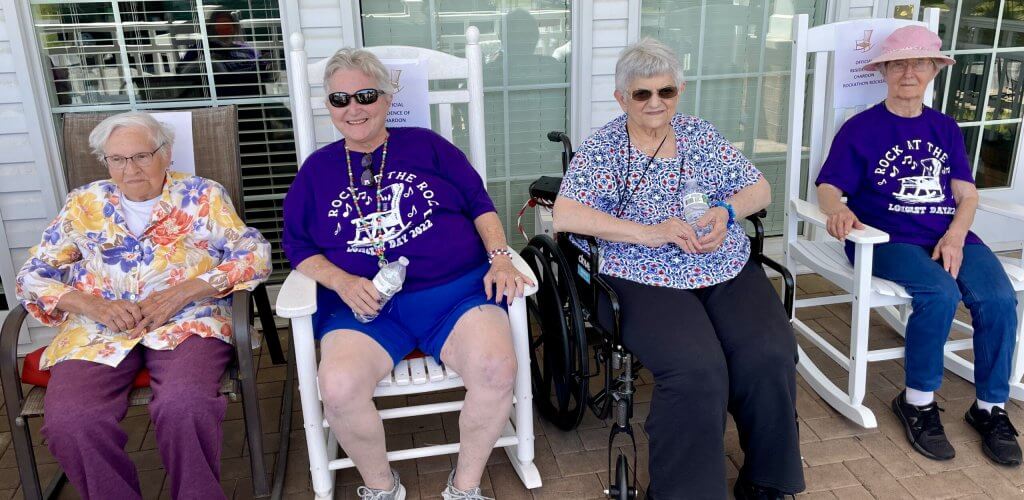 four senior women sit together outside on rocking chairs