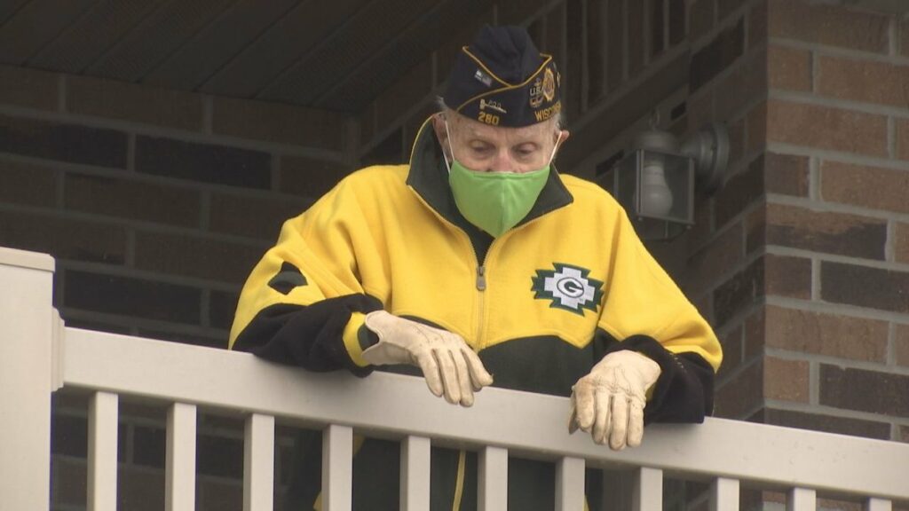 senior man with a mask on looks down from his apartment balcony