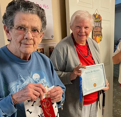 two senior women smile while holding an award