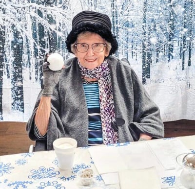 senior woman poses with a fake snowball and a winter backdrop
