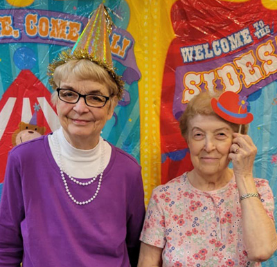 two senior women smile with props at a carnival-themed photo station