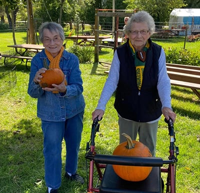 two senior women smile with their pumpkins at a pumpkin patch