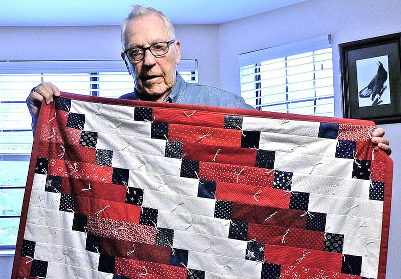 senior man holds an American-themed quilt