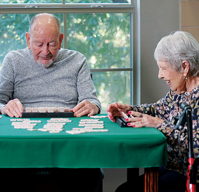 senior woman and senior man play dominoes together at a table in an independent living community