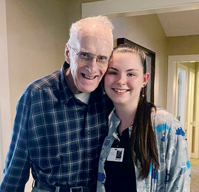 An assisted living resident and team member smiling and hugging in a community hallway.