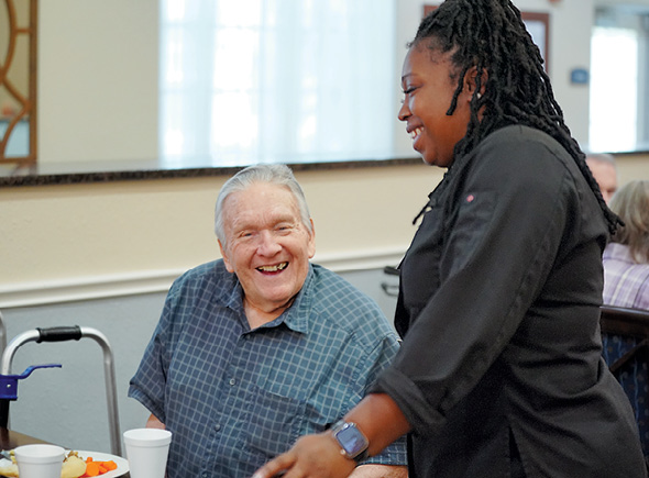 A smiling resident being served by a dining hall team member at a Sonida Senior Living assisted living community.