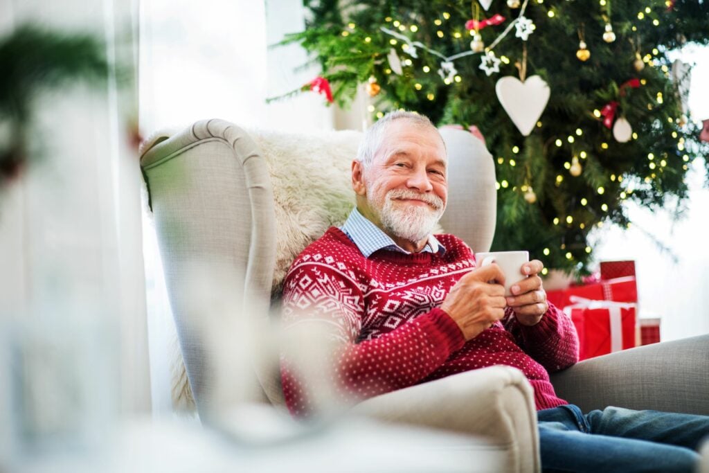 senior man with a cup sitting on armchair at home at Christmas time.