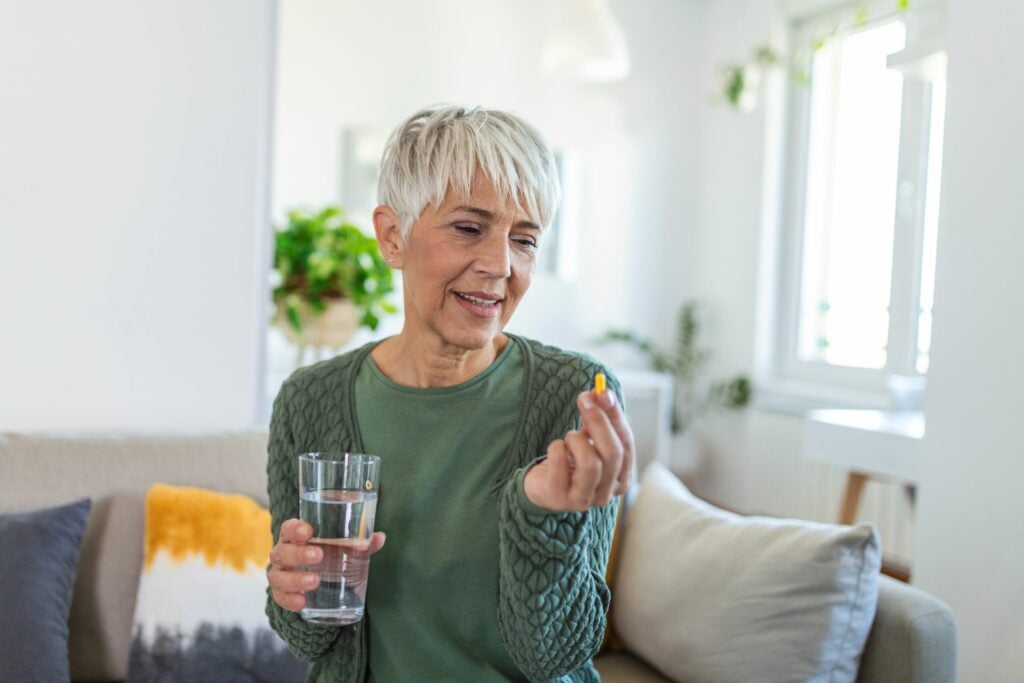 Smiling mature woman taking a vitamin sitting on sofa of in living room.