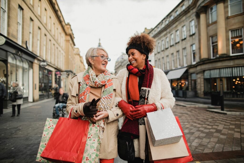 Two female adult friends walking through the city streets at Christmas. They are talking and smiling as they do some Christmas shopping.