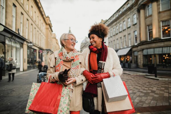 Two female adult friends walking through the city streets at Christmas. They are talking and smiling as they do some Christmas shopping.