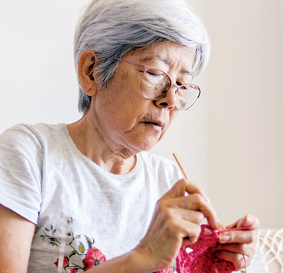 A senior woman focusing on a crochet project in an assisted living community managed by Sonida Senior Living.