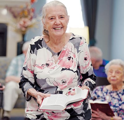 A resident holding a Bible and leading friends in a religious study at a Sonida Senior Living community.