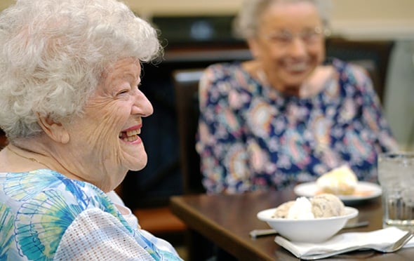 Two smiling female residents of a Sonida Senior Living assisted living community enjoy an ice cream social together at a table