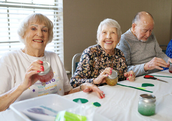 A smiling group of seniors showing off their completed art projects at an independent and assisted living community managed by Sonida Senior Living.