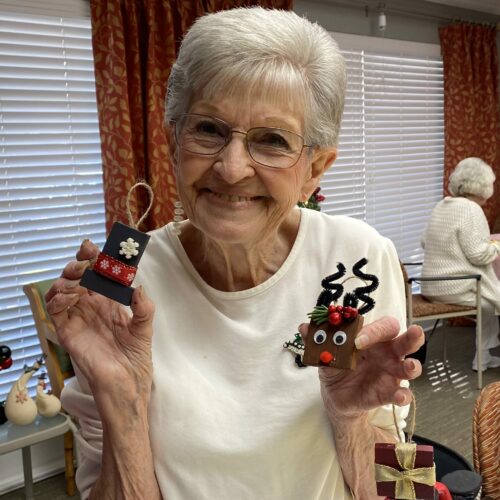 elderly woman smiles while holding her two homemade Christmas ornaments