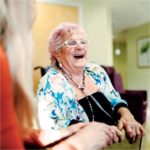 A pink haired senior woman laughing during a gathering at a Sonida Senior Living assisted living community.