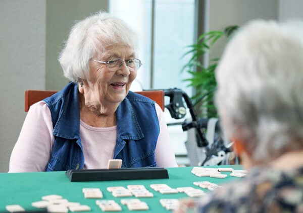 A smiling woman playing a game of dominos with fellow residents at a Sonida Senior Living independent and assisted living community.